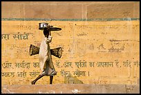 Man carrying a plater in front of wall with inscriptions in Hindi. Varanasi, Uttar Pradesh, India (color)