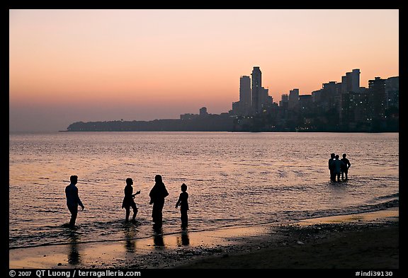 People standing in water at sunset with skyline behind, Chowpatty Beach. Mumbai, Maharashtra, India