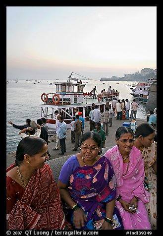 Women sitting on waterfront with boats behind at twilight. Mumbai, Maharashtra, India (color)