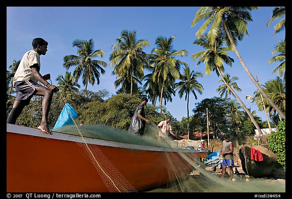 Men mending fishing net with palm trees in background. Goa, India