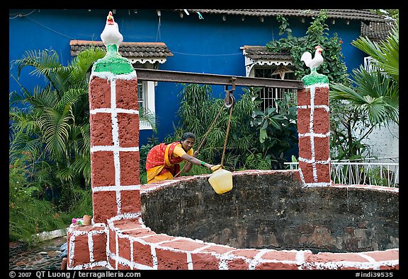Woman retrieving water from well with blue house behind, Panjim. Goa, India