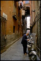 Man locking his motorbike in a side street. Naples, Campania, Italy (color)
