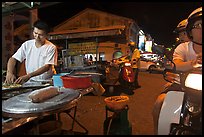 Man preparing food as people wait on motorbike. George Town, Penang, Malaysia (color)