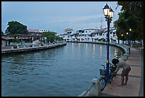 Woman locking bicyle on quay of Melaka River. Malacca City, Malaysia (color)