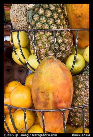 Boy peers from behind fruits offered at a juice stand, Tlaquepaque. Jalisco, Mexico