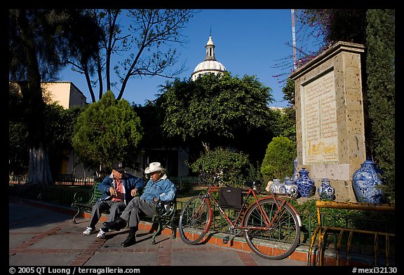 Men sitting in garden, with cathedral dome and ceramic monument, Tlaquepaque. Jalisco, Mexico
