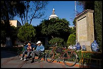 Men sitting in garden, with cathedral dome and ceramic monument, Tlaquepaque. Jalisco, Mexico ( color)