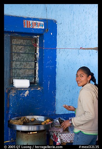 Woman preparing food outside a blue wall, Tonala. Jalisco, Mexico (color)