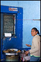 Woman preparing food outside a blue wall, Tonala. Jalisco, Mexico