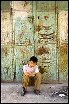 Young boy sitting in front of a closed store, Hebron. West Bank, Occupied Territories (Israel) (color)