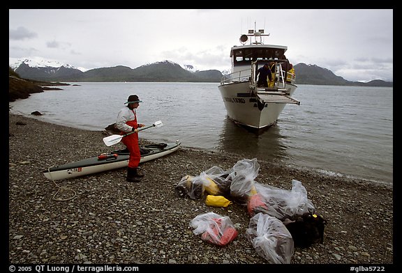 Kayaker standing with gear wrapped in plastic bags after drop-off. Glacier Bay National Park, Alaska (color)