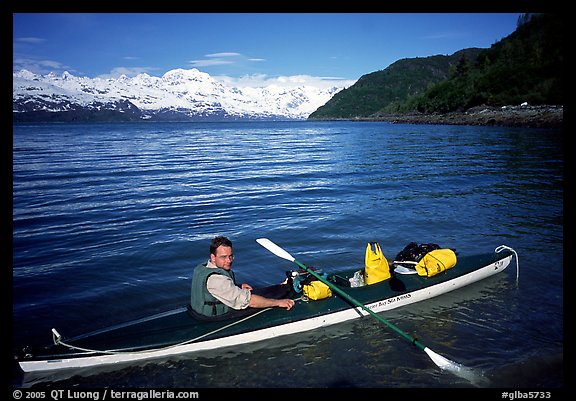 Kayaker sitting at a rear of a double kayak with the Fairweather range in the background. Glacier Bay National Park, Alaska