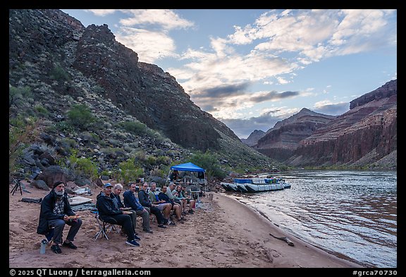 Group of river rafters seated on a sandy beach having dinner near their camp on the Colorado River. Grand Canyon National Park, Arizona (color)