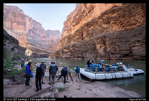 Group of rafters loading gear to a motorized raft at a sandy landing beneath towering Grand Canyon cliffs. Grand Canyon National Park, Arizona (color)