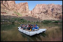 Motorized raft loaded with passengers floats through calm waters of the Colorado River surrounded by towering Grand Canyon cliffs. Grand Canyon National Park, Arizona ( color)