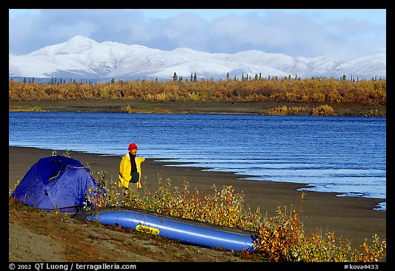 Canoeist standing next to tent and canoe with snowy mountains in the background. Kobuk Valley National Park, Alaska (color)