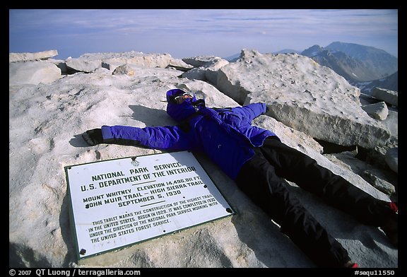 Hiker laying exhausted on Mt Whitney summit sign. California (color)