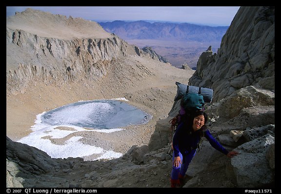 Woman with backpack pausing on steep terrain above Iceberg Lake. California
