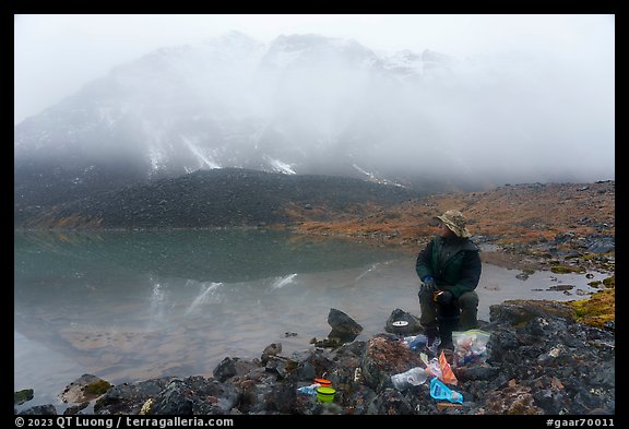 Backpacker eating near lake with foggy mountain. Gates of the Arctic National Park, Alaska, USA.