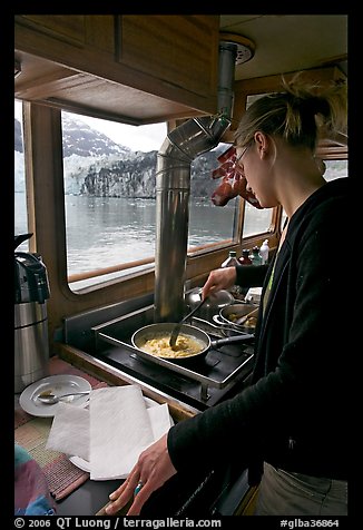 Woman cooking eggs aboard small tour boat, with glacier outside. Glacier Bay National Park, Alaska, USA.