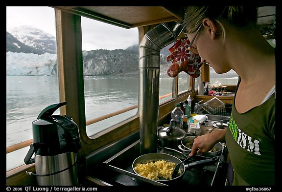 Woman prepares breakfast eggs aboard small tour boat, with glacier in view. Glacier Bay National Park (color)