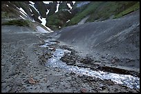 Stream flows from verdant hills into  barren valley floor. Katmai National Park, Alaska, USA. (color)