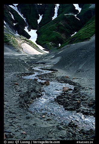 Stream flows from the verdant hills into the barren floor of the Valley of Ten Thousand smokes. Katmai National Park, Alaska, USA.