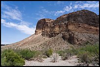Volcanic cliffs rise steeply above a sparsely vegetated wash under a bright desert sky. Big Bend National Park ( color)