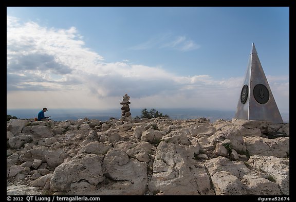 Hiker sitting on Guadalupe Peak summit with cairn and monument. Guadalupe Mountains National Park, Texas, USA.