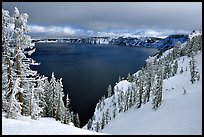 Trees and lake in winter with clouds and dark waters. Crater Lake National Park, Oregon, USA.