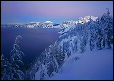 Snow-covered rim and trees, lake and mountains, dusk. Crater Lake National Park, Oregon, USA.