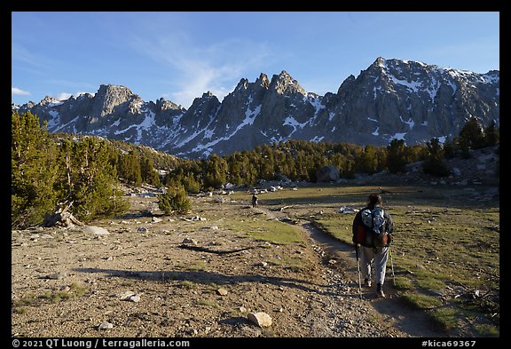 Backpackers walking on trail in meadow towards mountains. Kings Canyon National Park, California, USA.