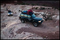 4WD vehicles driving over rock at dusk in Teapot Canyon. Canyonlands National Park, Utah, USA. (color)