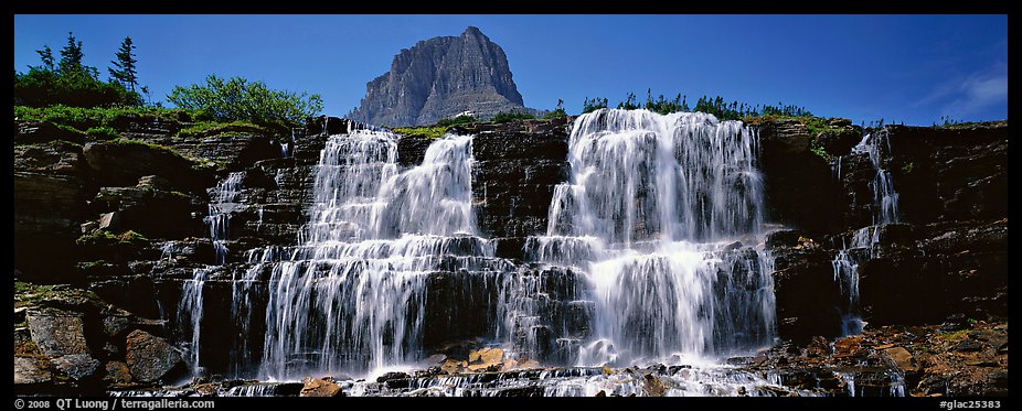 Waterfall flowing over dark rock and peak. Glacier National Park, Montana, USA.