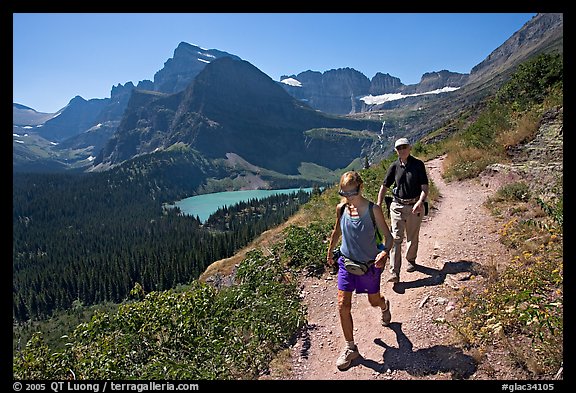 Couple hiking on trail, with Grinnell Lake below. Glacier National Park, Montana, USA.