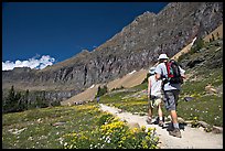 Hikers on trail amongst wildflowers near Hidden Lake. Glacier National Park, Montana, USA.