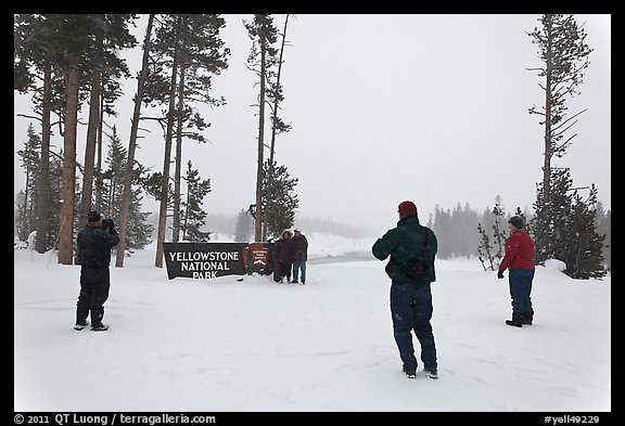 Visitors take pictures with entrance sign in winter. Yellowstone National Park, Wyoming, USA.