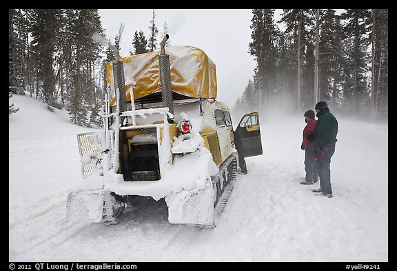 Couple standing in snowdrift next to snow coach. Yellowstone National Park, Wyoming, USA.