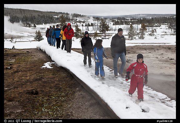 Tourists walk over snow-covered boardwalk. Yellowstone National Park, Wyoming, USA.