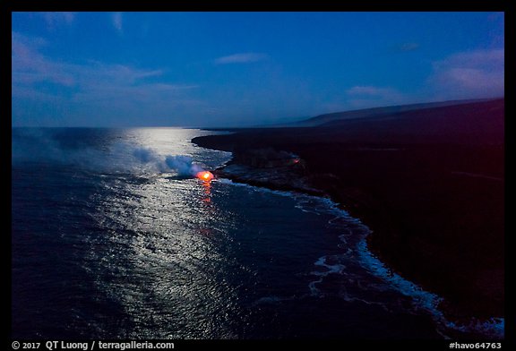 Aerial view of coastline with distant lava ocean entry and moonlight reflections at night. Hawaii Volcanoes National Park, Hawaii, USA.