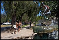 Young men carring surfboards next to statue of surfer, Kapiolani Park. Waikiki, Honolulu, Oahu island, Hawaii, USA