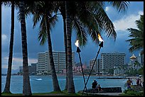 Waterfront at dusk with bare flame lamps. Waikiki, Honolulu, Oahu island, Hawaii, USA (color)