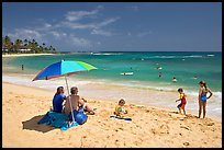 Couple sitting under sun unbrella with children playing around, Poipu Beach, mid-day. Kauai island, Hawaii, USA ( color)