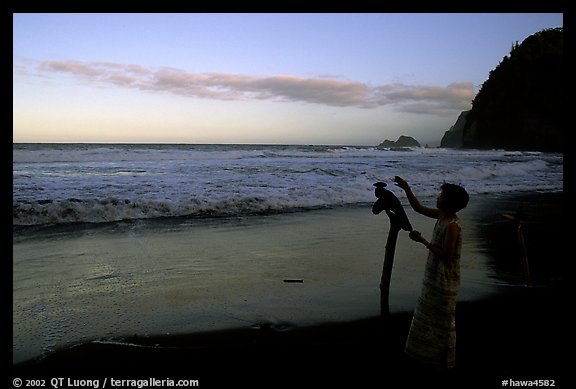 Hawaiian woman piles a stone on a stick as a traditional gesture of reverence, Polulu Beach. Big Island, Hawaii, USA