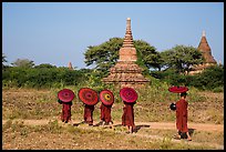Buddhist Novices with red sun umbrellas on path near old stupas. Bagan, Myanmar ( color)