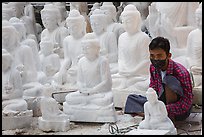 Man working amongst many  buddha statues on Marble street workshop. Mandalay, Myanmar ( color)