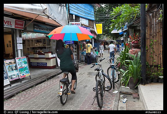 Woman riding bicycle with unbrella, Tonsai village, Ko Phi-Phi Don. Krabi Province, Thailand (color)