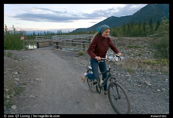 Woman on mountain bike with bridge behind. McCarthy, Alaska, USA (color)