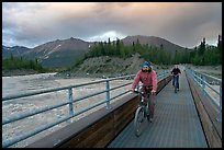 Mountain bikers crossing Kennicott River Footbridge at sunset. McCarthy, Alaska, USA