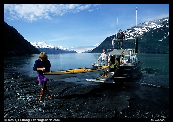Man and woman carry kayak out of small boat at Black Sand Beach. Prince William Sound, Alaska, USA (color)